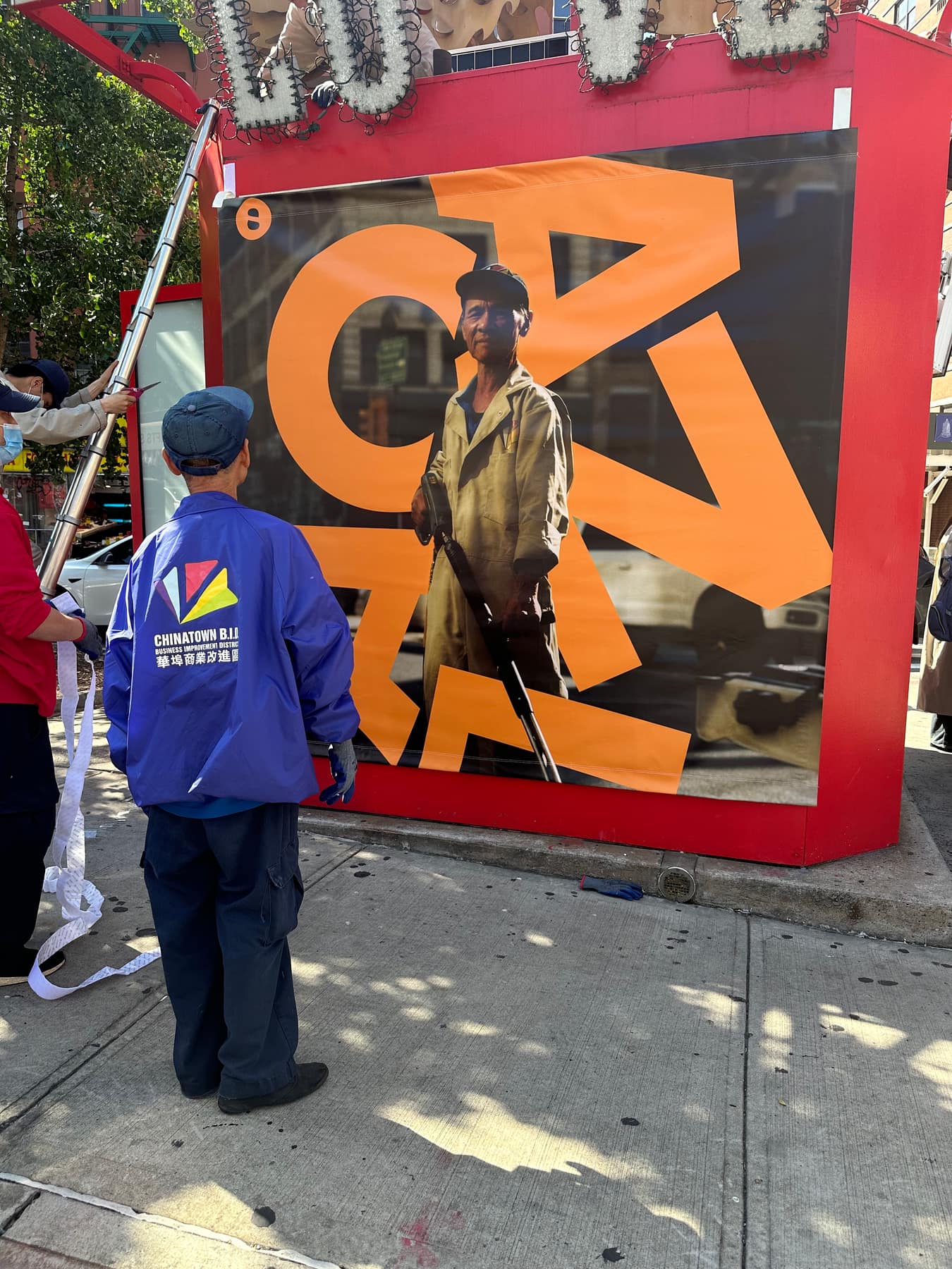 A Chinatown Partnership worker in a blue jacket at the red information booth, the orange CANAL banner behind him