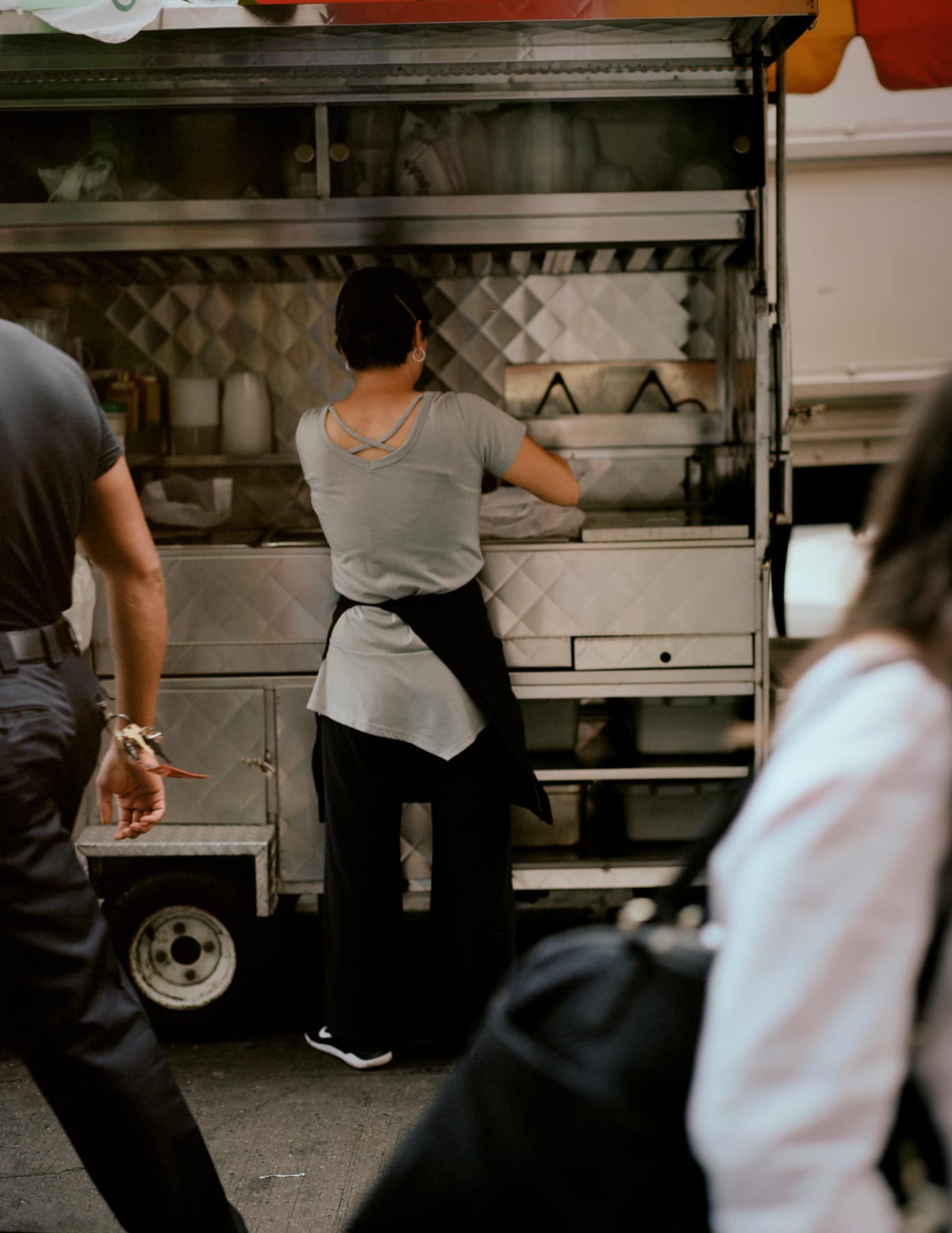 A vendor loading a food truck, seen between two people passing on the sidewalk