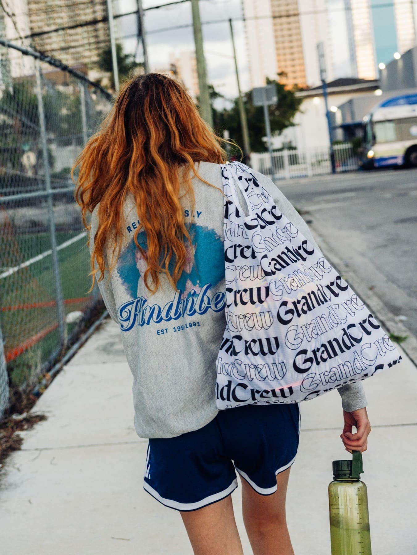 A woman walking a city block with the Grand Crew tote over her shoulder