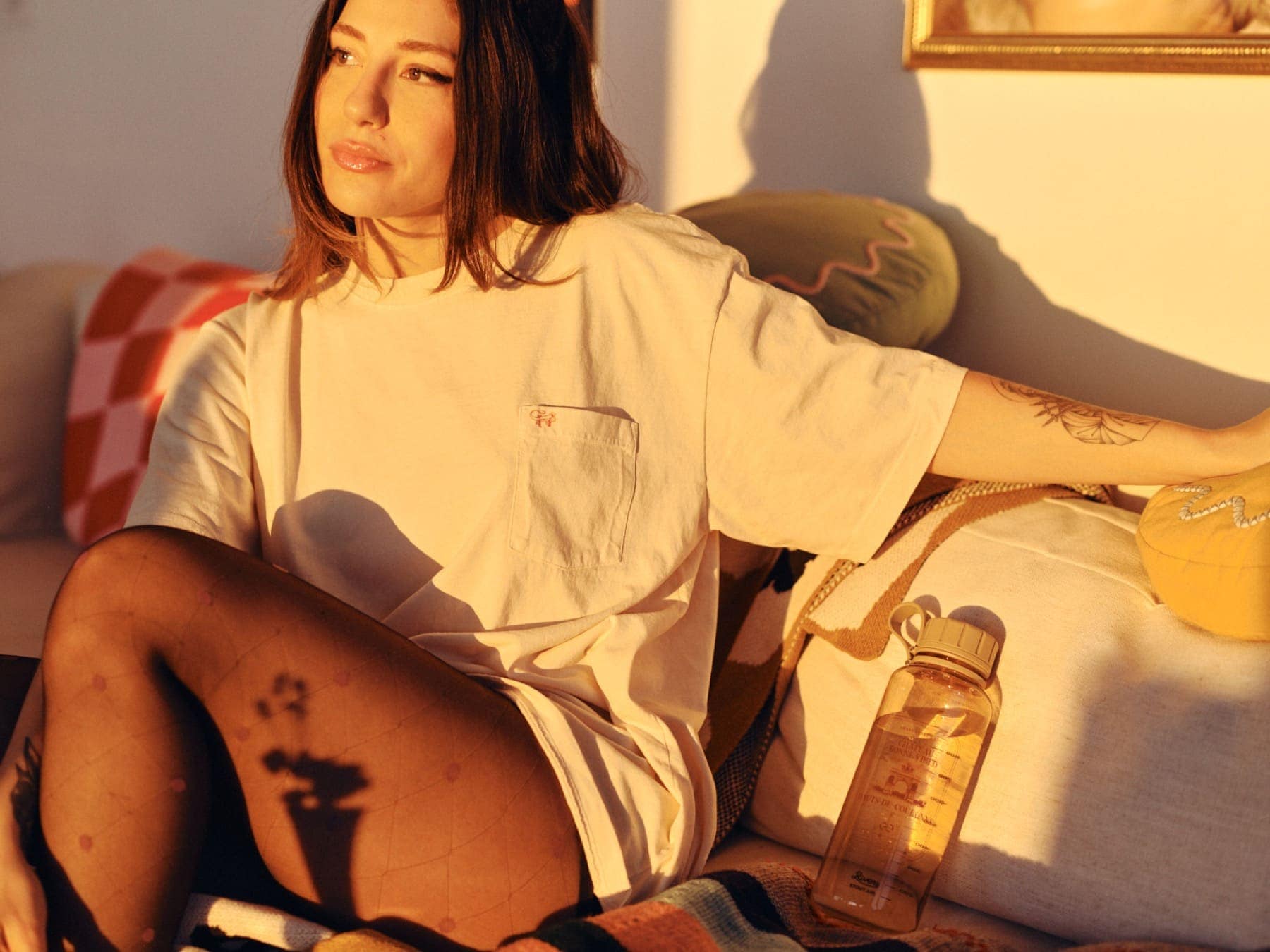 A woman on a couch in evening light wearing the cream tee