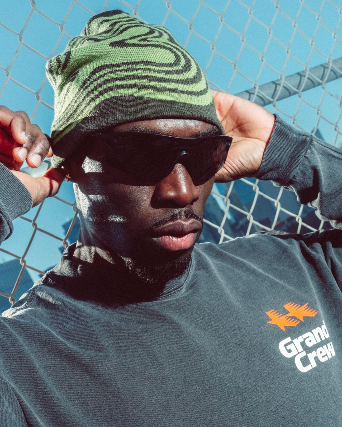 The beanie and sunglasses against a chain-link fence