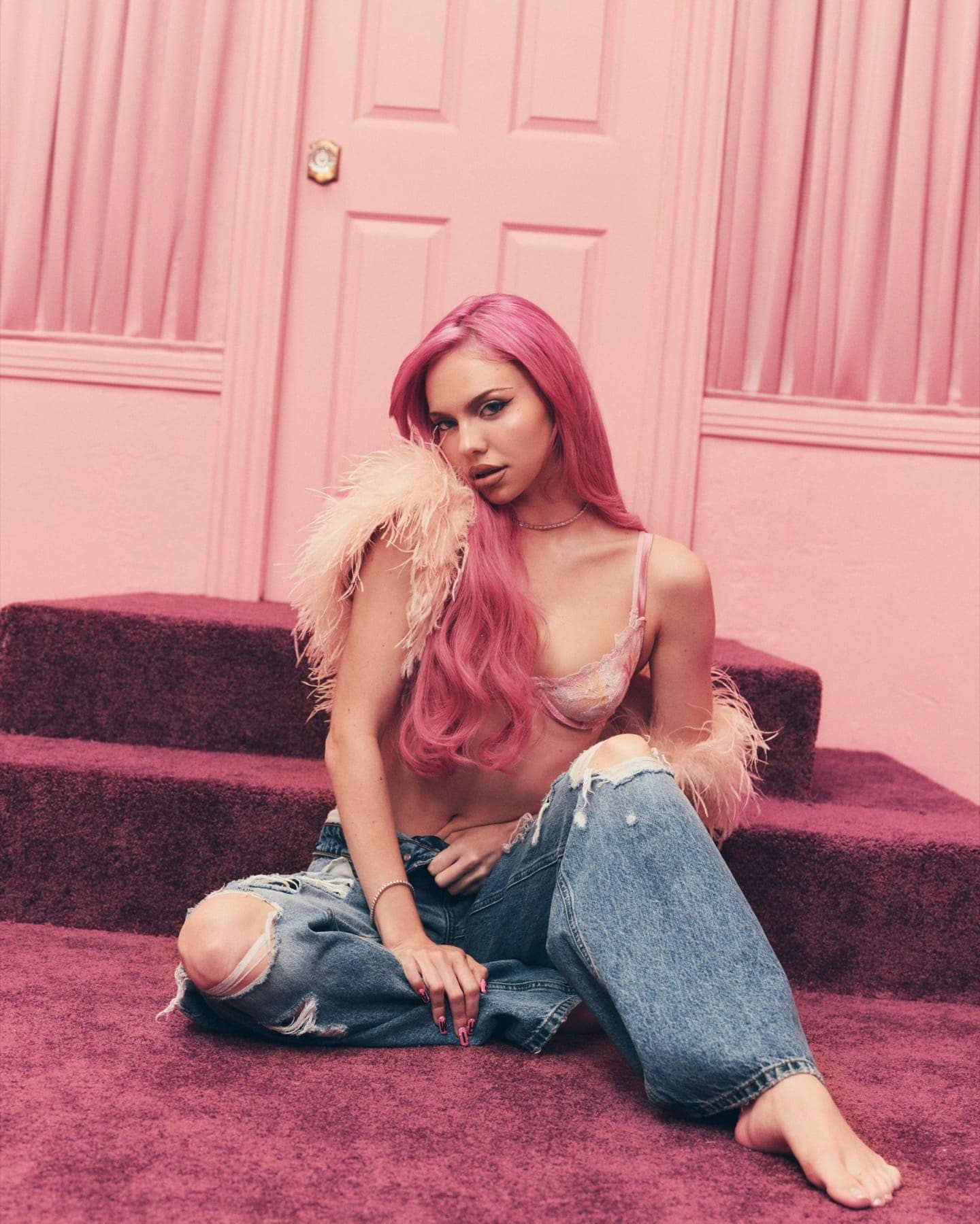 ADÉLA seated on carpeted pink steps in jeans and feathers