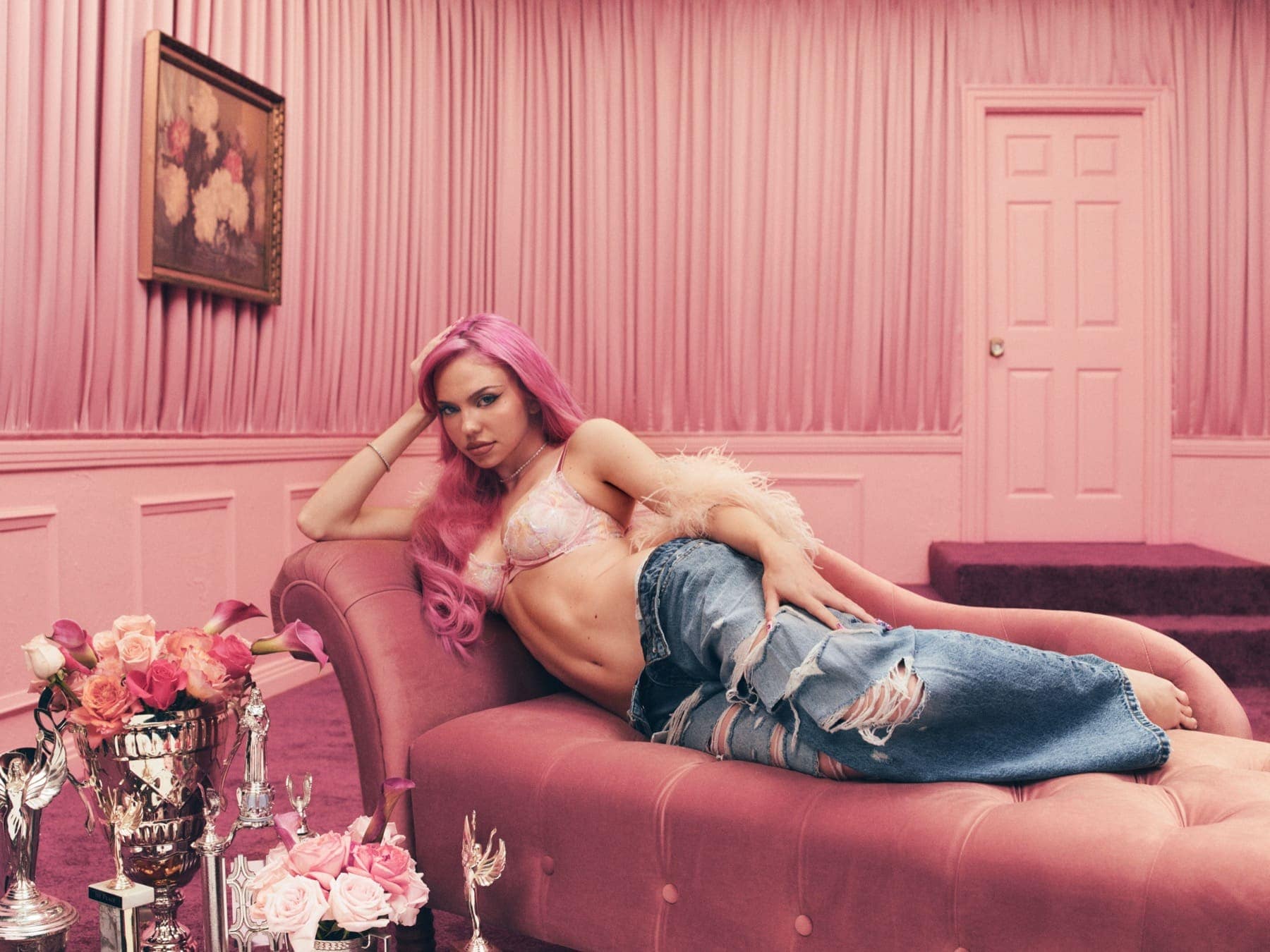 ADÉLA lying on a pink velvet couch in a pink room, flowers and trophies in the foreground