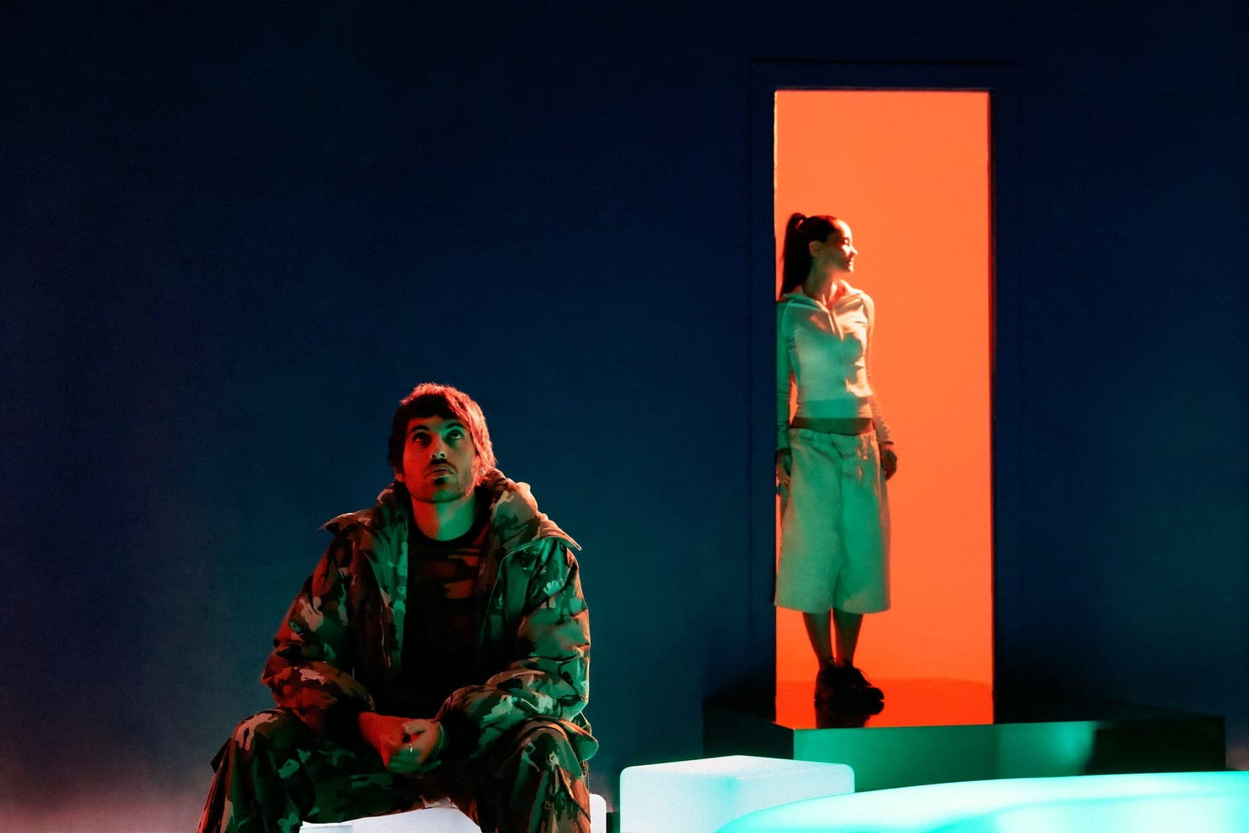 Jackson Walker Lewis seated in green light with Shanny Wise framed in an orange doorway behind him