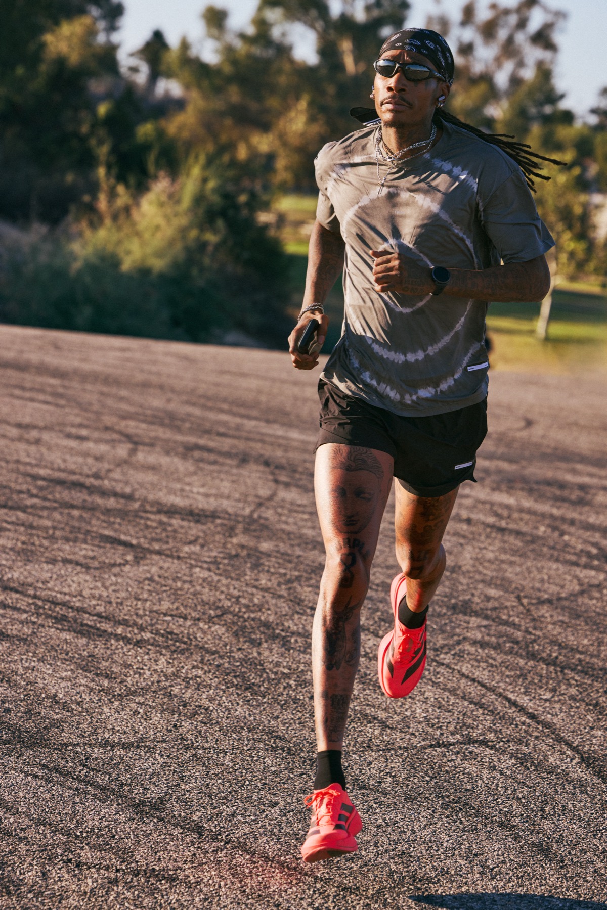 Wiz Khalifa running toward camera on a hilltop road in the Running Mode tee and red shoes