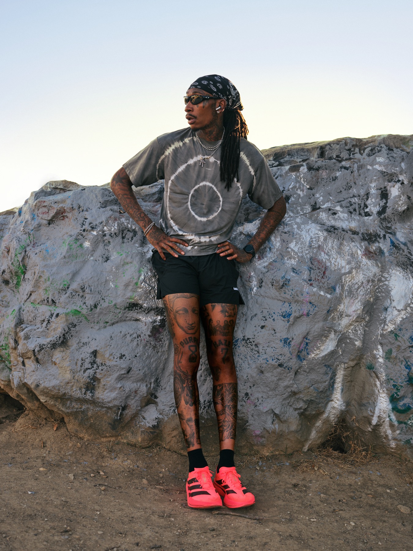 Wiz Khalifa leaning on a painted boulder, hands on hips, the city behind