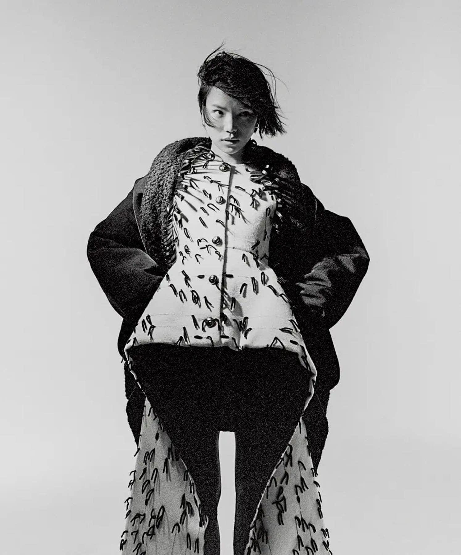 Model in an oversized dark coat over a feather-print dress, shot in black and white