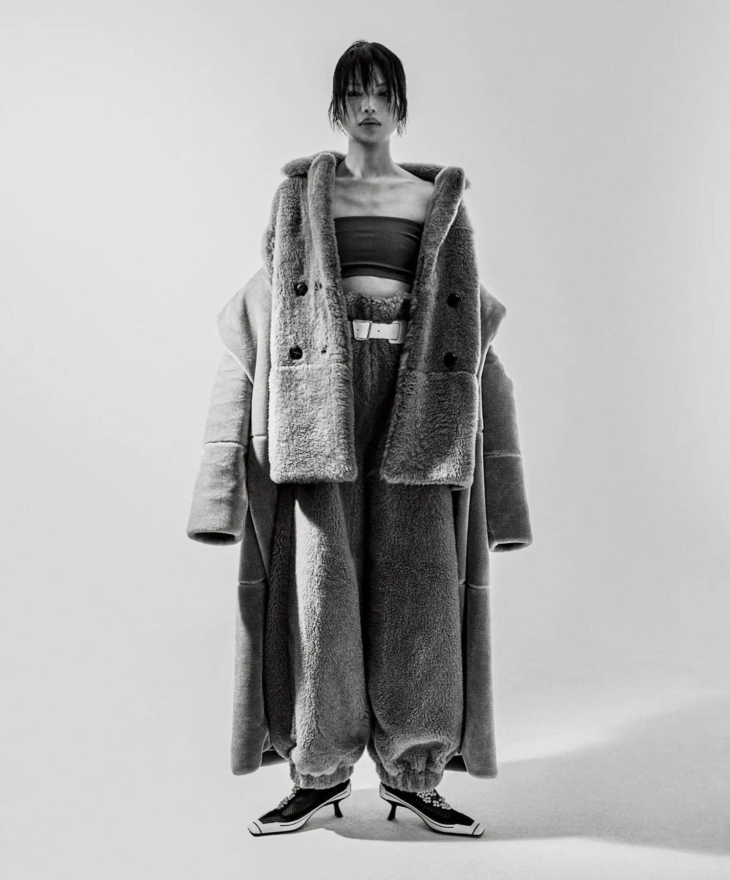 Model in an oversized grey shearling coat and matching trousers over a black bandeau