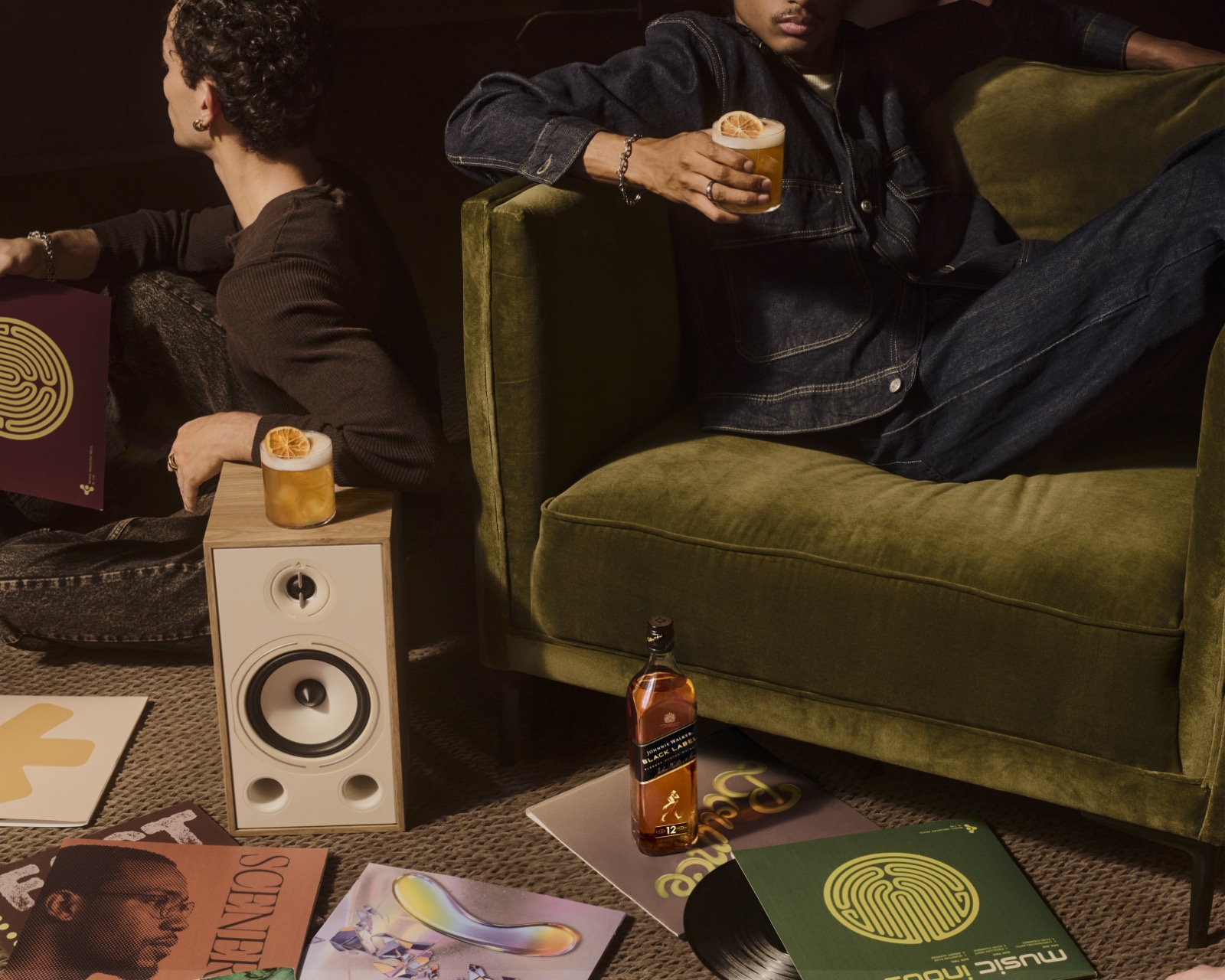 Two women at a gold-lit round table locking eyes over a Johnnie Walker Black Label serve