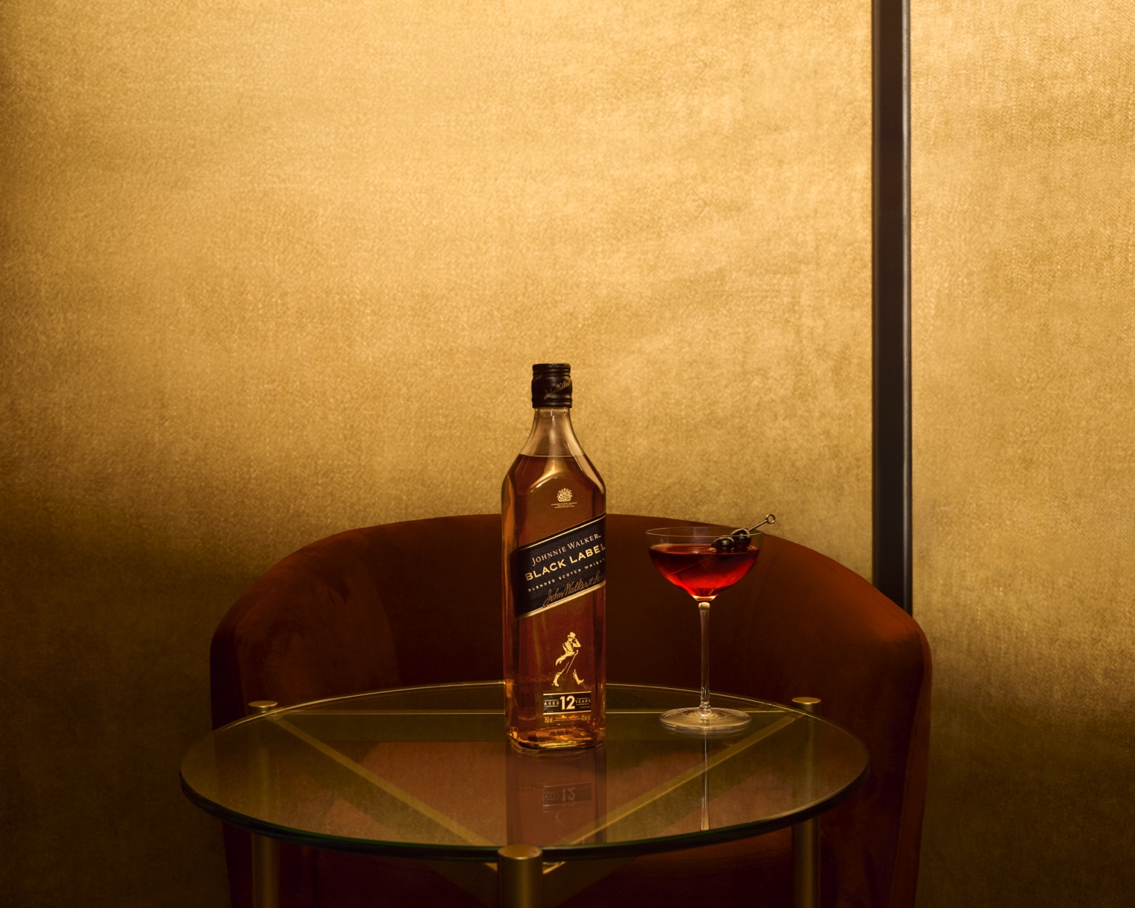 A Johnnie Walker bottle and coupe glass on a round table against a glowing gold wall